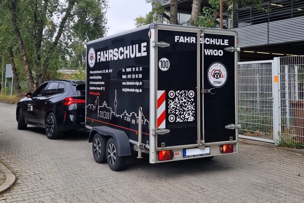 Schwarzes Auto mit einem Anhänger der Fahrschule WiGo in Berlin.